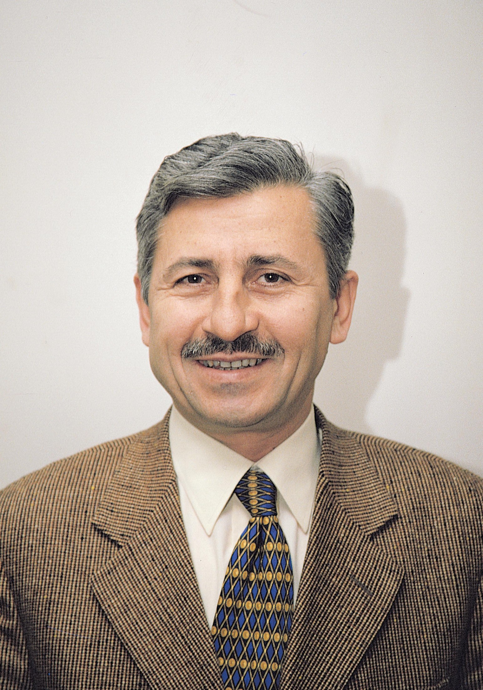 Mehmet Oruç’un kahverengi ceketli gülümseyen portresi
